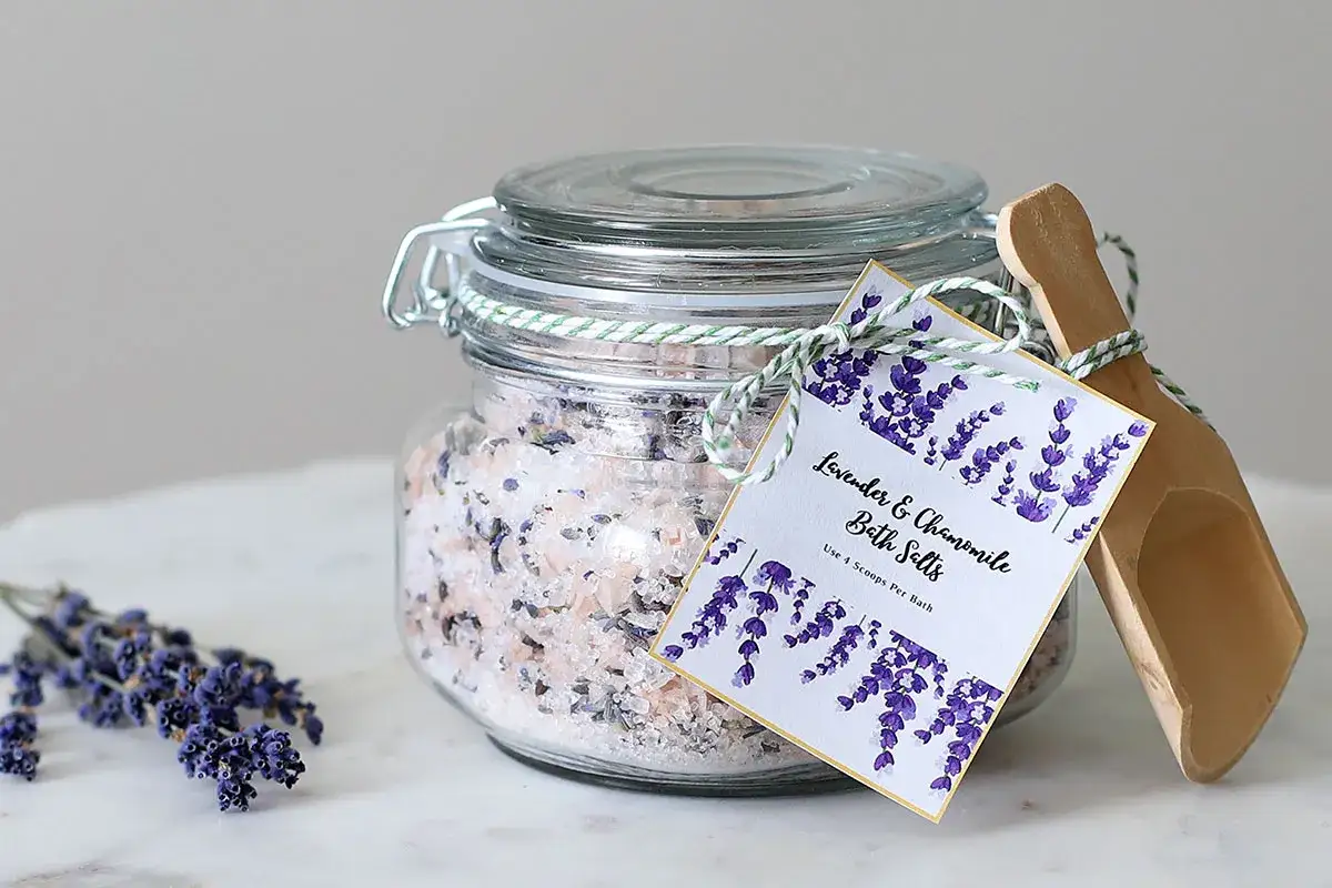 Selbstgemachtes Lavendel-Kamille-Badesalz im Glas mit Holzschaufel und frischen Lavendelzweigen. Perfekt zum Entspannen.