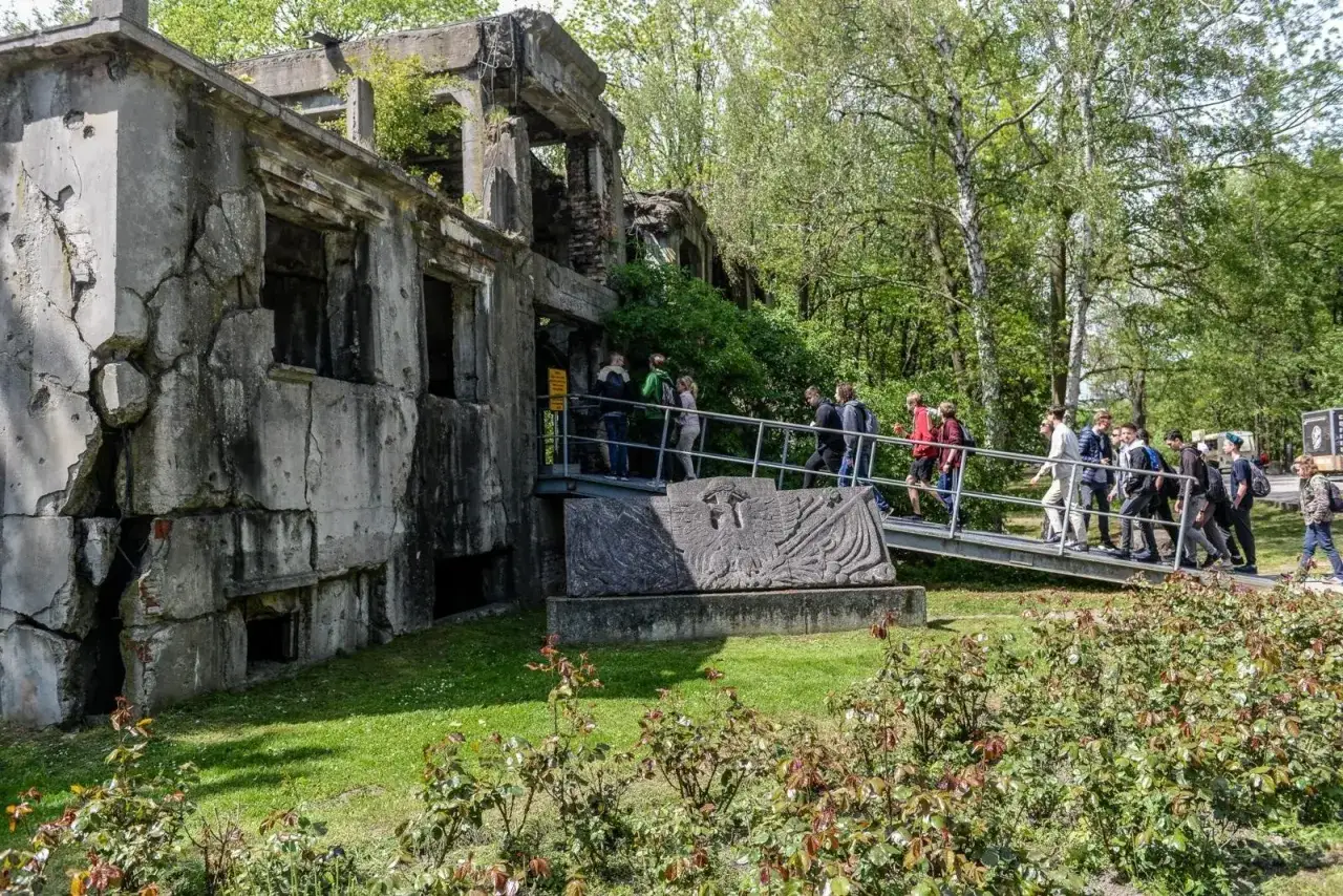 Ruiny koszar na Westerplatte. Grupa turyst&oacute;w wchodzi na kładkę. Warto zobaczyć to miejsce pamięci.