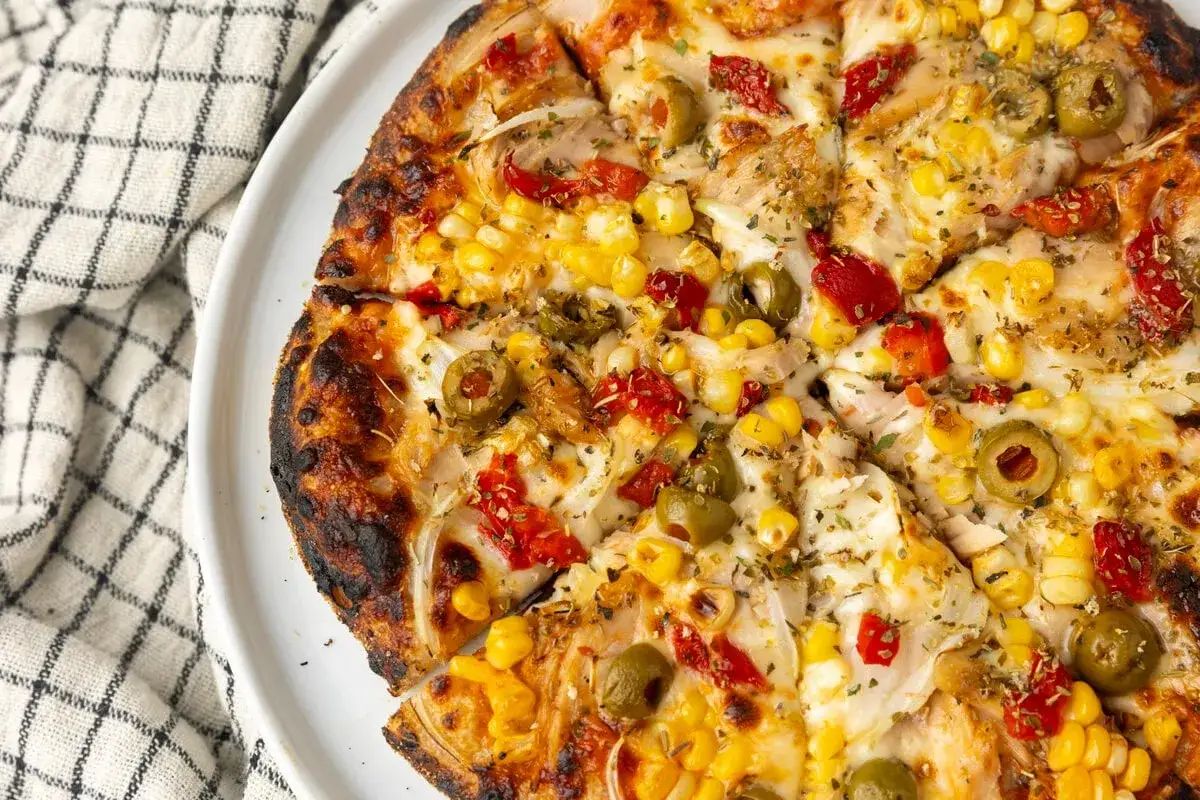 Pyszna pizza z tuńczykiem, kukurydzą, oliwkami i papryką, z chrupiącym, lekko przypieczonym brzegiem.