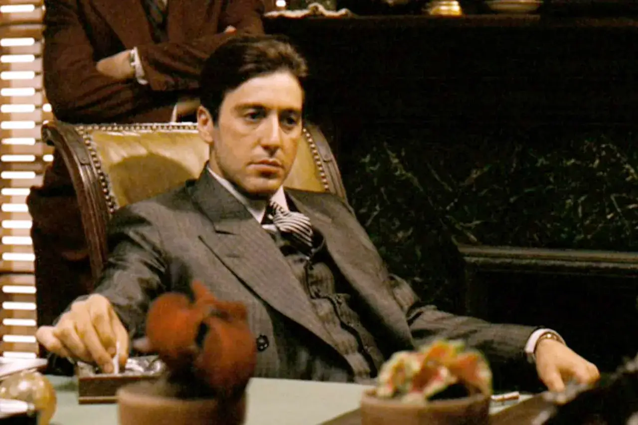 Al Pacino som Michael Corleone i filmer med al pacino, sitter i en läderstol och tar en cigarett.