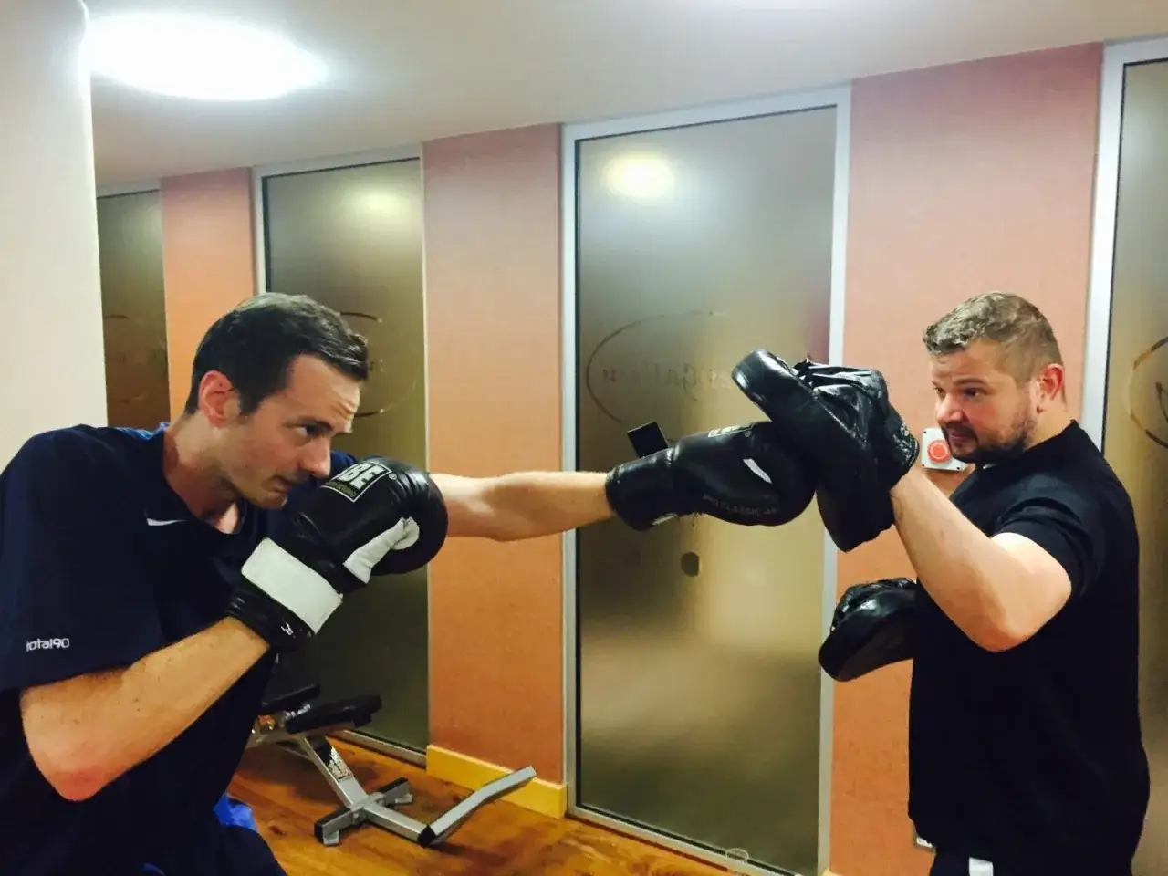 A boxer throws a jab punch at a trainer holding mitts.