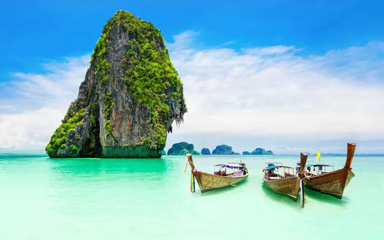 Trzy łodzie kołyszą się na turkusowej wodzie przy skalistej wyspie porośniętej zielenią. Rajskie widoki z Phuket, Tajlandia.