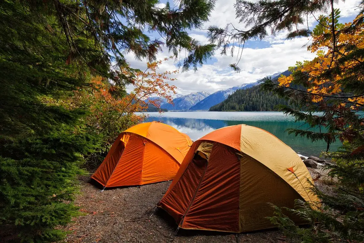 Tv&aring; orange t&auml;lt st&aring;r uppst&auml;llda vid en sj&ouml;, omgivna av h&ouml;stf&auml;rgad skog och berg. En perfekt plats f&ouml;r kamlunge camping.