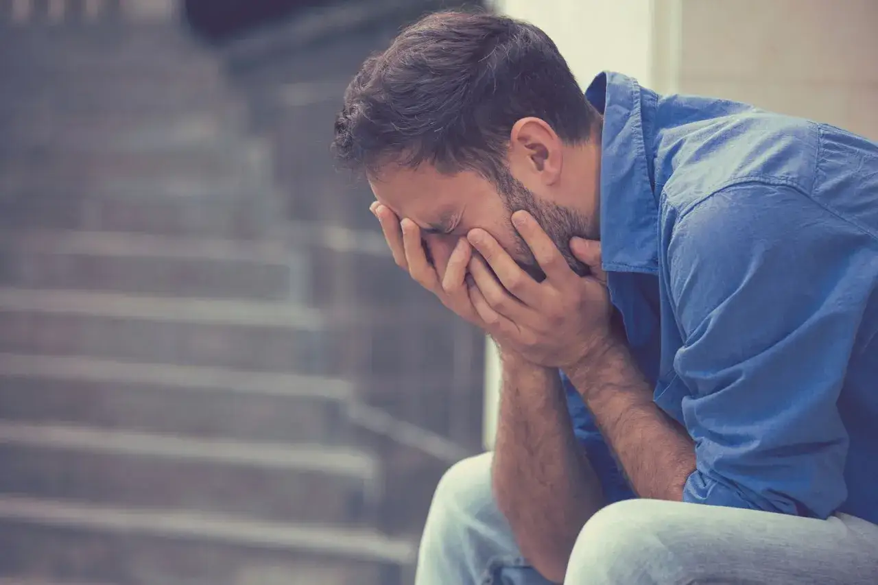 Uomo seduto sulle scale, con le mani sul viso, che riflette su cosa succede se piangi troppo.