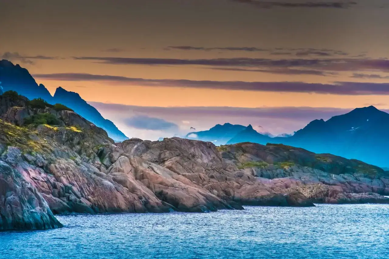 Klippor och berg vid havet i Nordnorge, en dr&ouml;m f&ouml;r fiske. Solnedg&aring;ngens f&auml;rger speglas i vattnet.