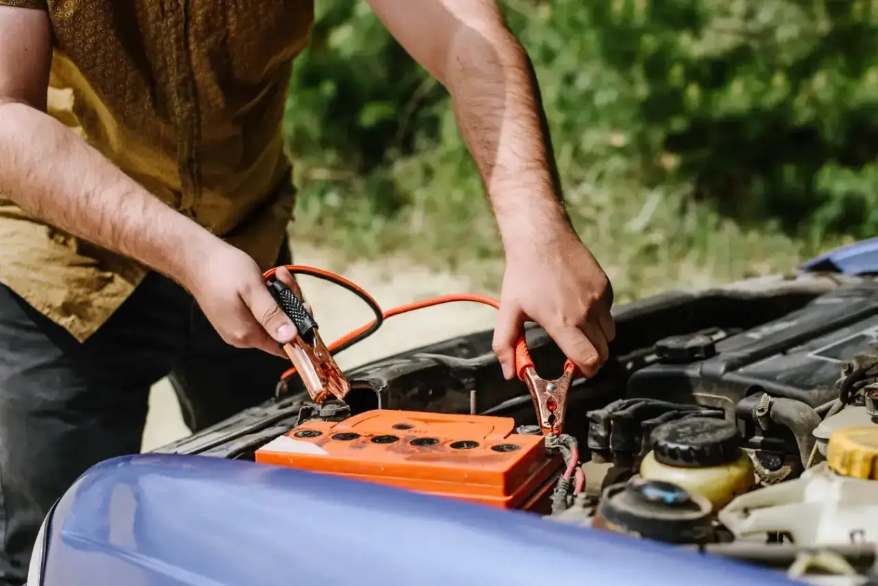 Hombre conectando pinzas a la batería del coche para comprobar su estado.