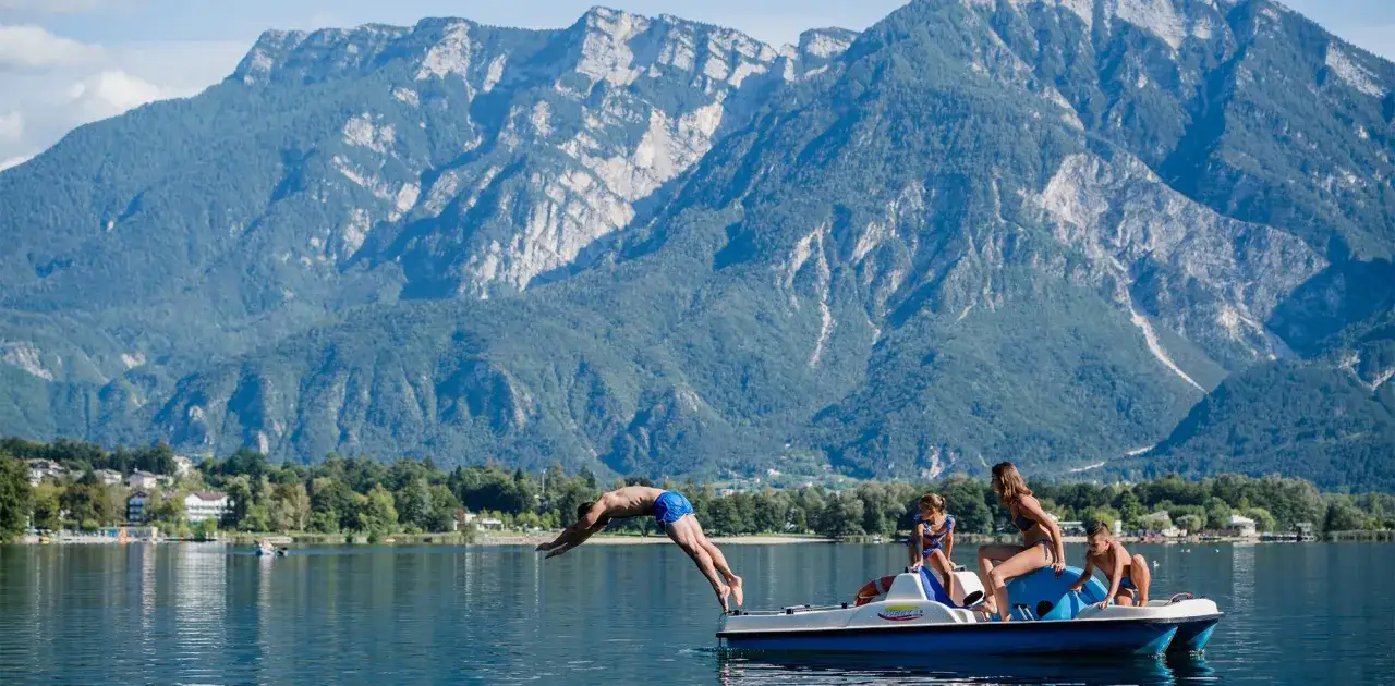 Un tuffo rinfrescante dal pedalò sul lago di Levico, con la spiaggia e le montagne sullo sfondo.