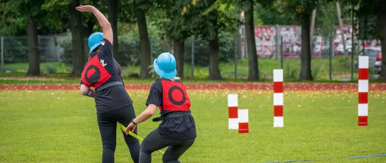 Dziewczyny w niebieskich kaskach i czerwonych kamizelkach biorą udział w zawodach OSP bojówka.