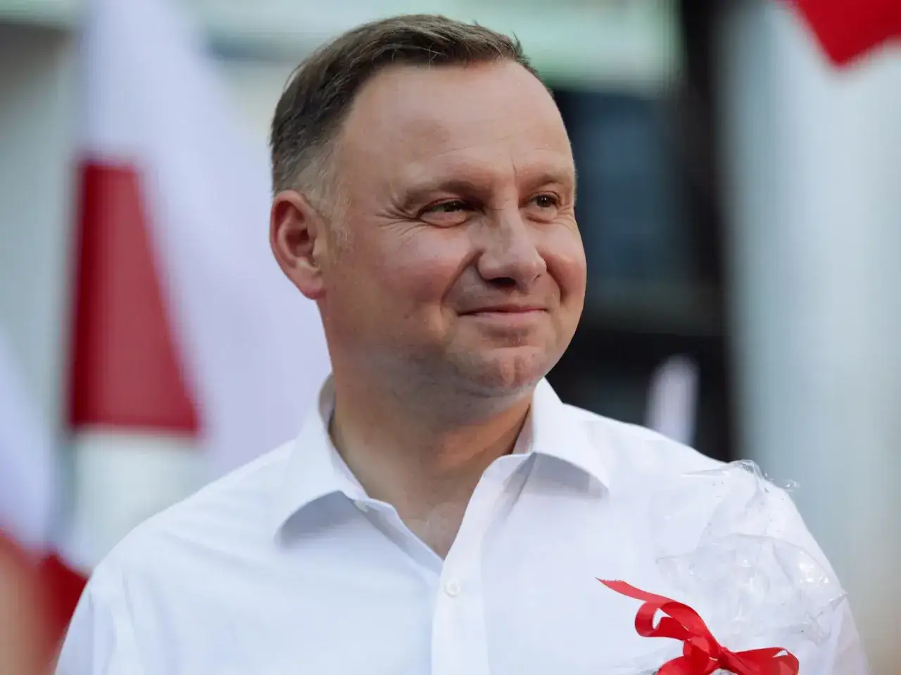 Uśmiechnięty mężczyzna w białej koszuli, z biało-czerwoną flagą w tle. Czyżby to zapowiedź spokojnej emerytury prezydenckiej?