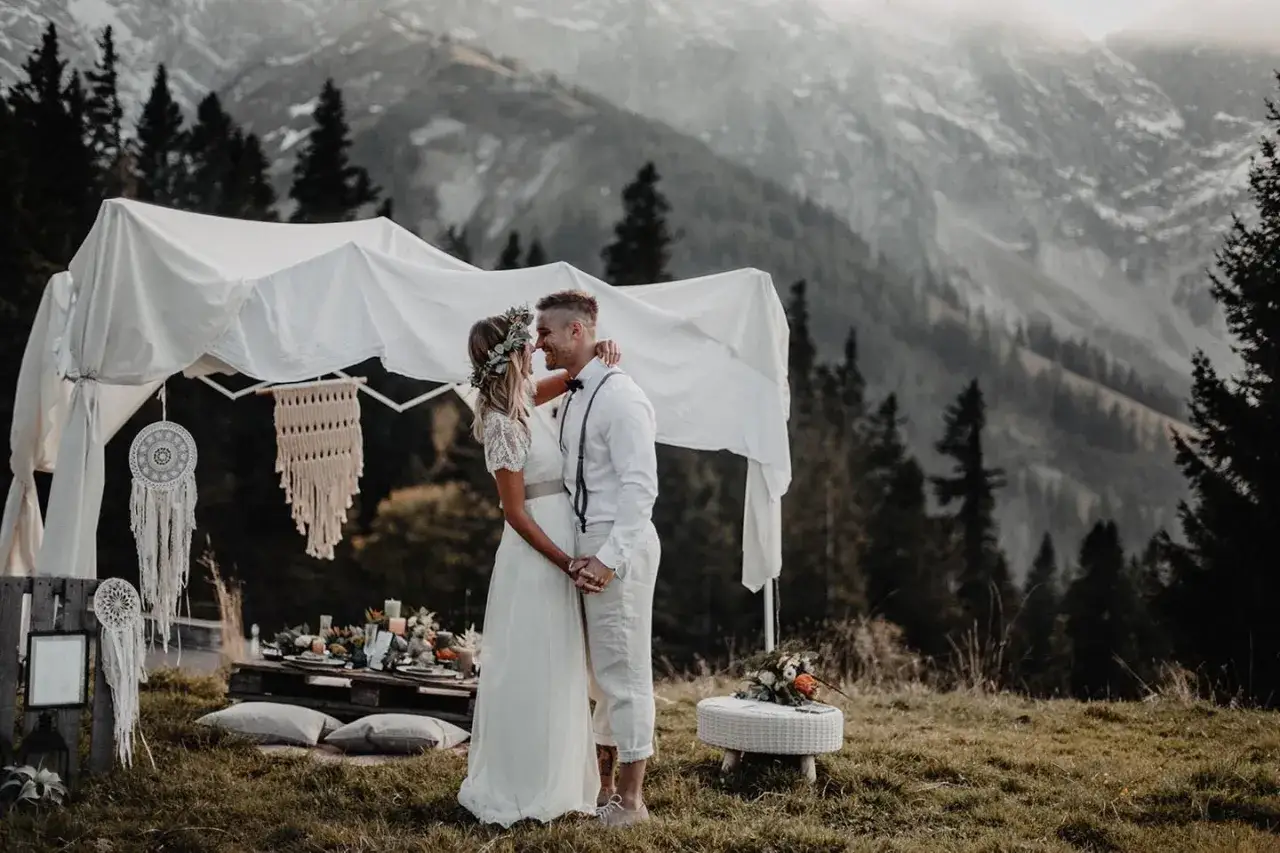Ein Brautpaar umarmt sich unter einem Baldachin, umgeben von der majestätischen Kulisse einer Hochzeit in den Bergen.