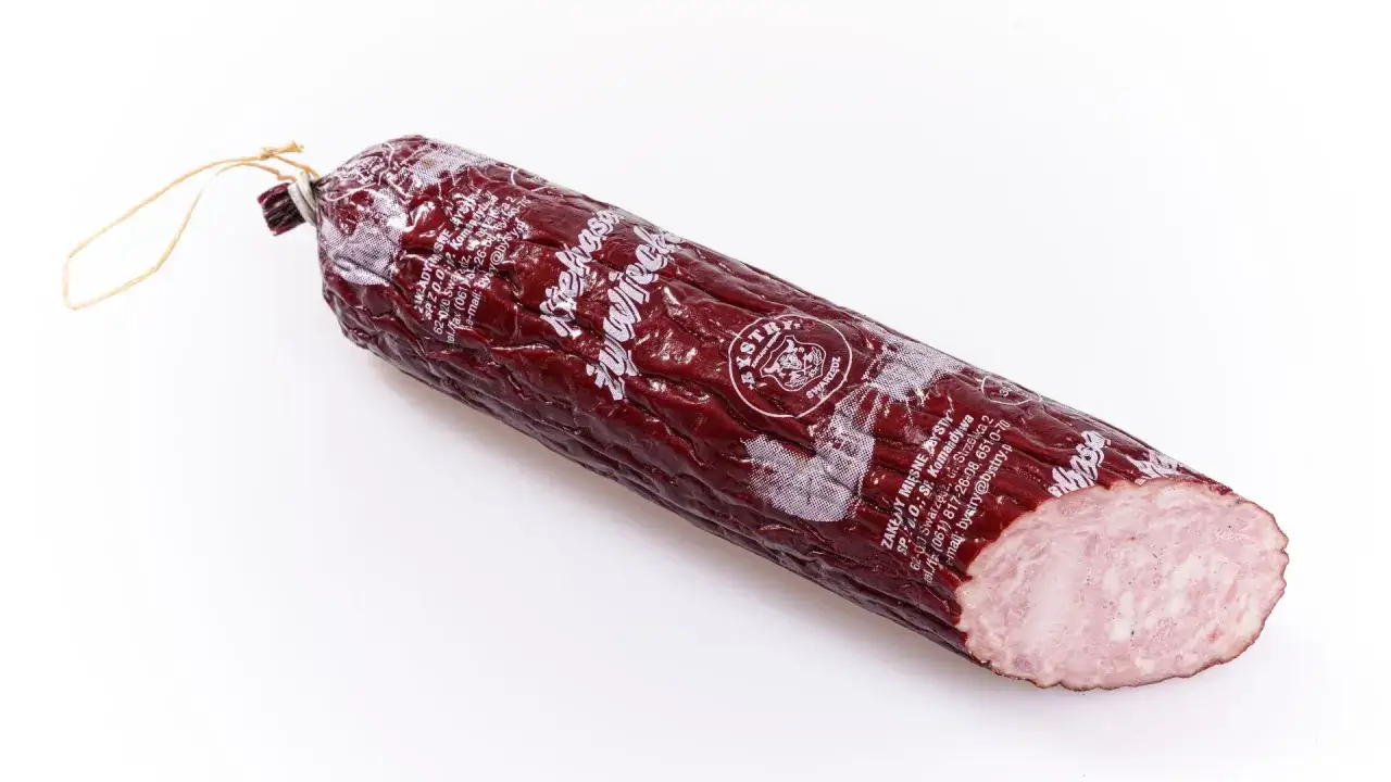 Kiełbasa żywiecka, wędzona, z widocznym przekrojem ukazującym jej delikatną strukturę. Zapakowana w ciemną osłonkę z białym nadrukiem.