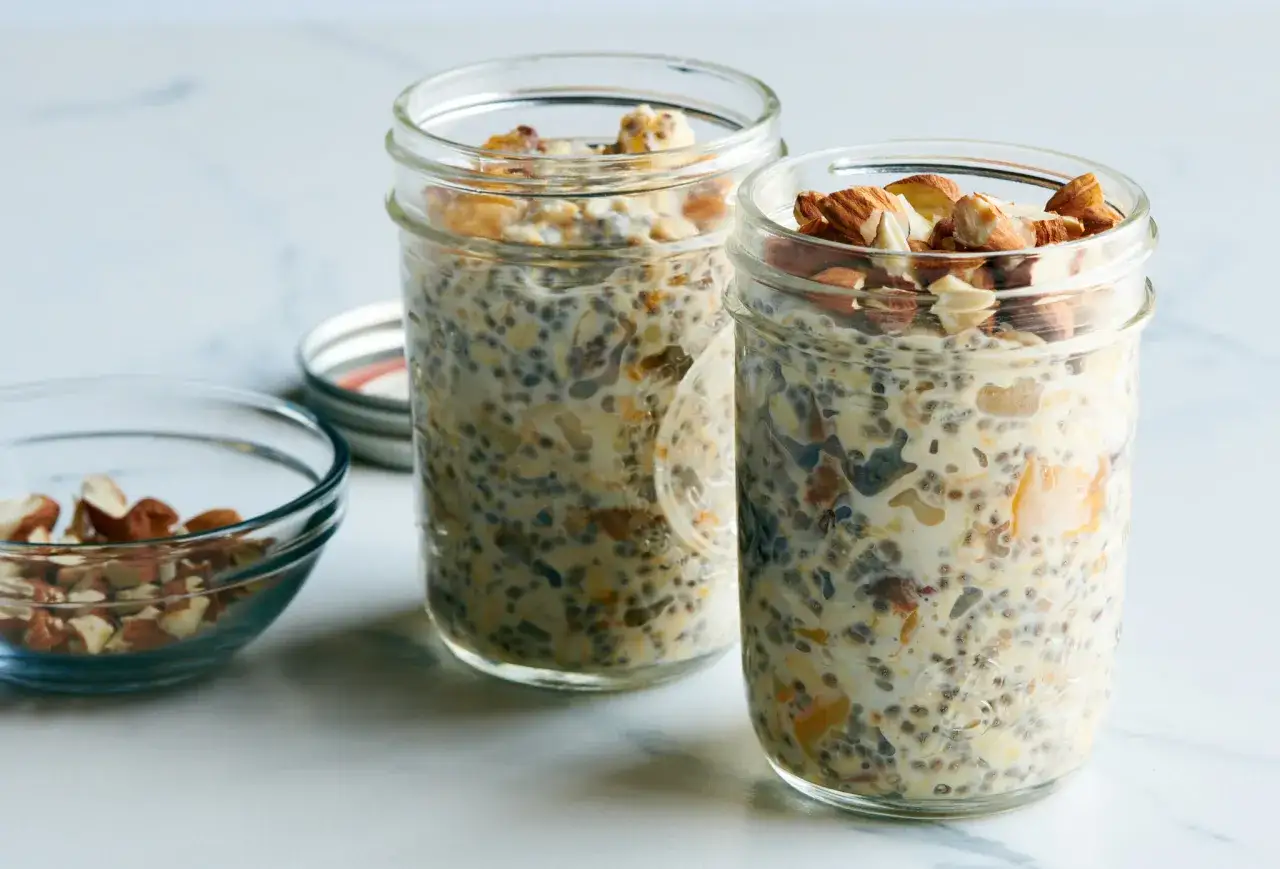 Dos frascos de avena nocturna con almendras picadas y un taz&oacute;n peque&ntilde;o con m&aacute;s almendras.