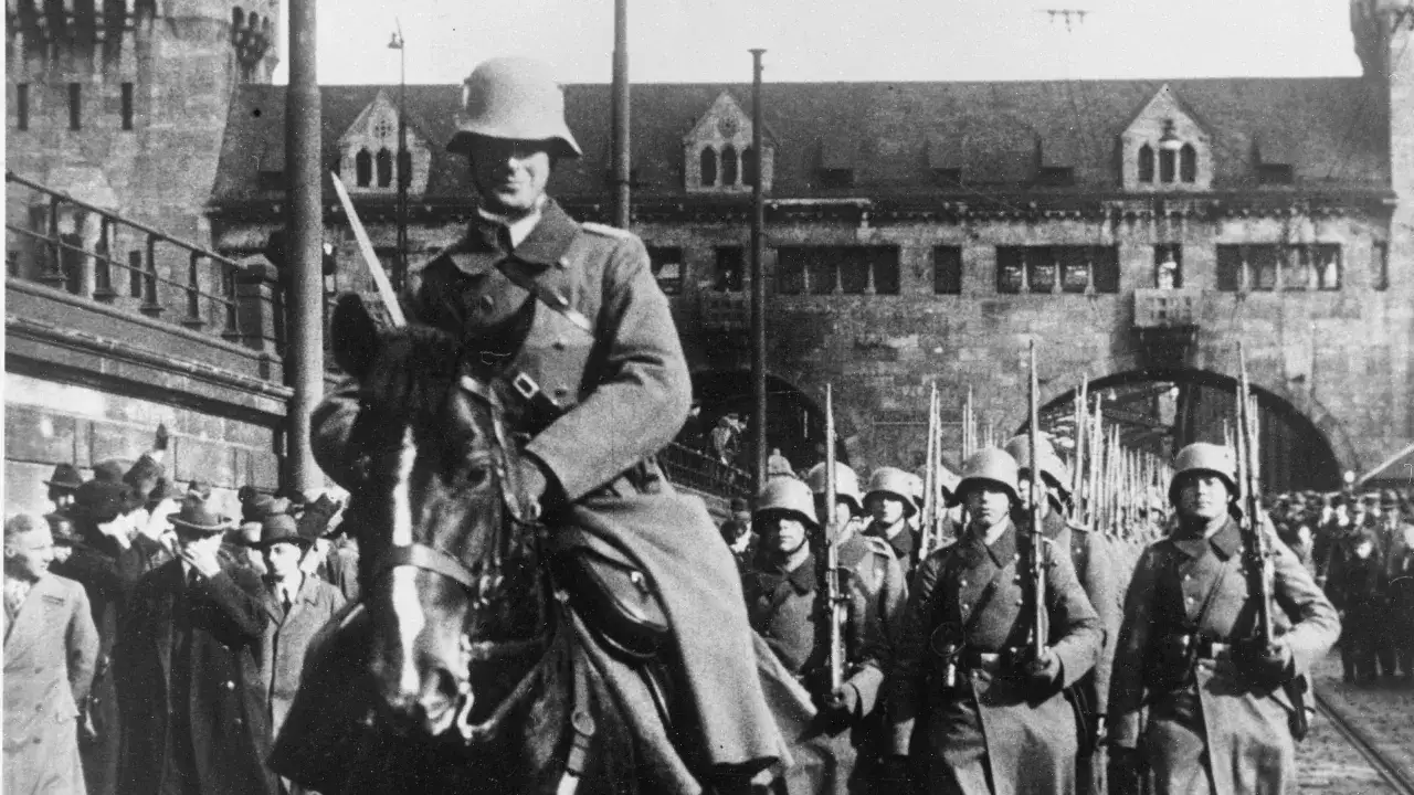 Soldaten marschieren im Rahmen der Rheinlandbesetzung 1936. Ein Offizier zu Pferd führt die Truppe an.
