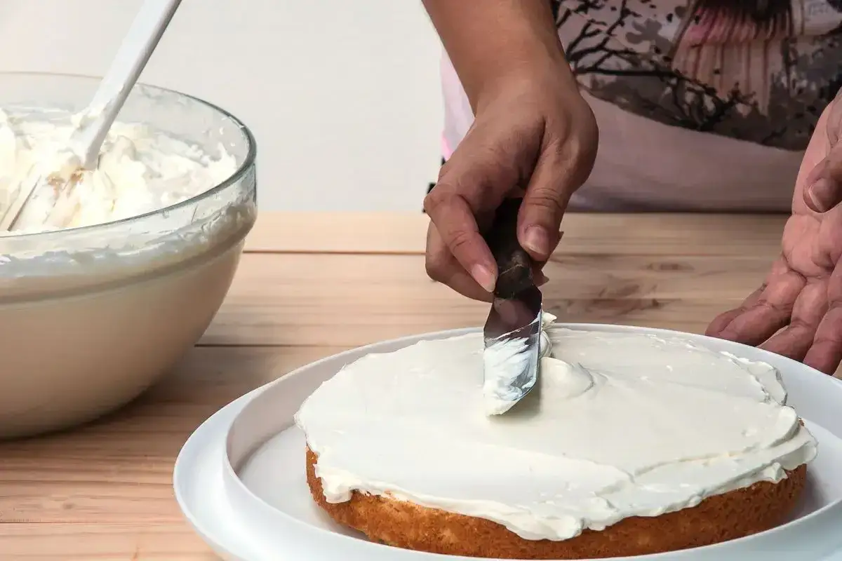 Mani esperte spalmano una soffice crema al burro su una torta, creando un dolce capolavoro.