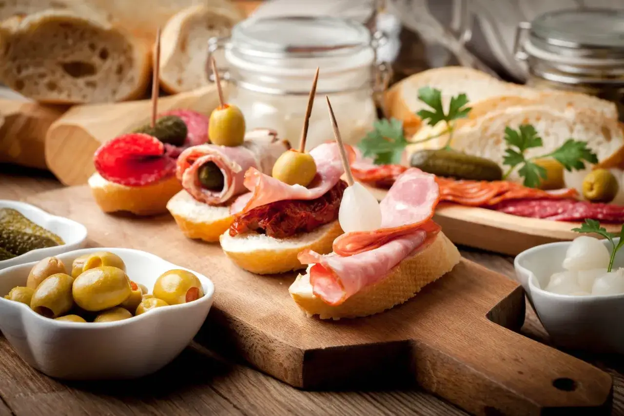 Pyszne tapas na drewnianej desce: kanapki z wędliną, oliwkami, suszonymi pomidorami i ogórkami.