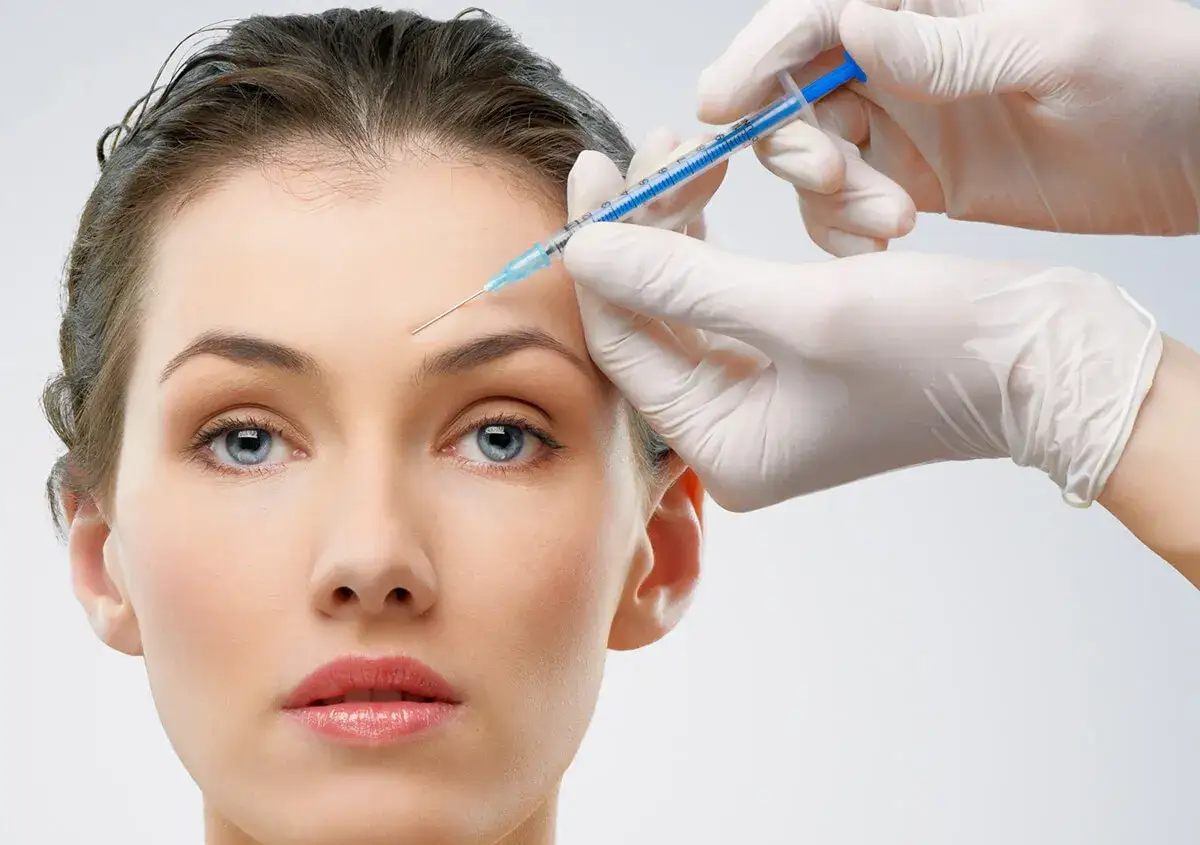 Eine Hand in einem wei&szlig;en Handschuh injiziert Botox in die Stirn einer Frau f&uuml;r ein glatteres Aussehen.