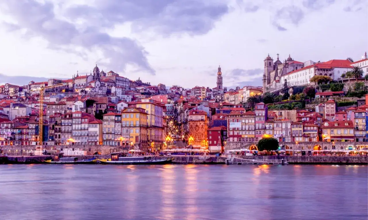 Kolorowe kamienice Porto, drugiego miasta Portugalii, odbijają się w rzece Douro o zmierzchu.