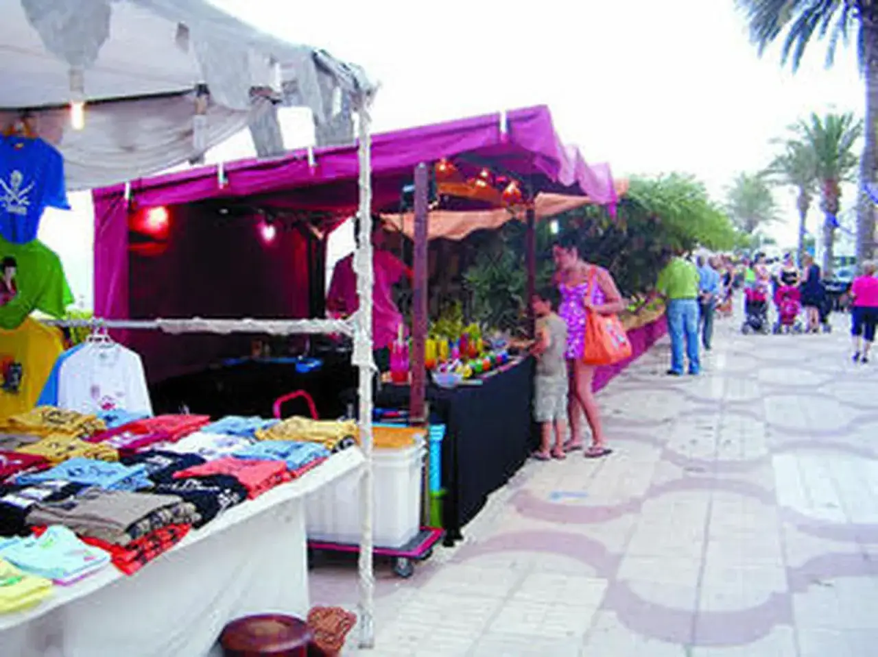 Paseo marítimo de Garrucha con puestos de ropa y souvenirs. Gente paseando y comprando bajo palmeras.