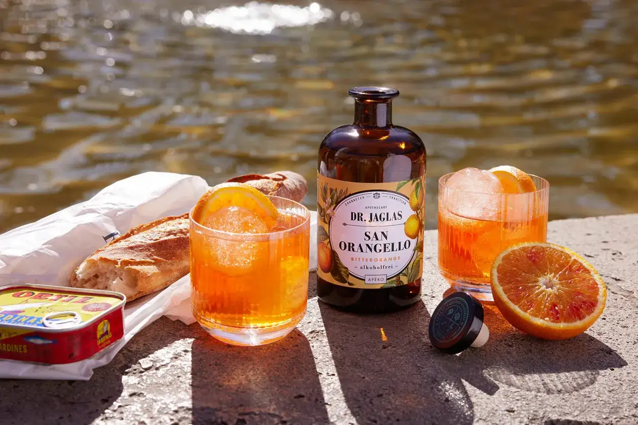 Erfrischender alkoholfreier Aperol mit Orangen garniert, dazu Baguette und Sardinen am Wasser.