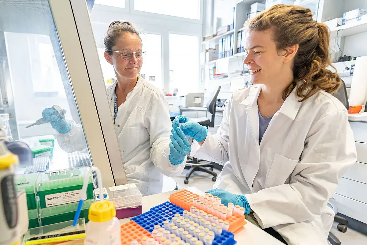 Zwei Wissenschaftlerinnen im Labor, eine studentische Hilfskraft h&auml;lt R&ouml;hrchen.