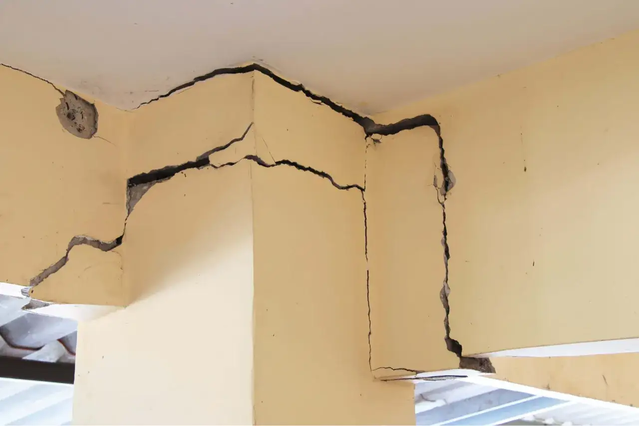 Gros plan sur une fissure horizontale traversant le coin d'un mur de maison, révélant la structure interne.