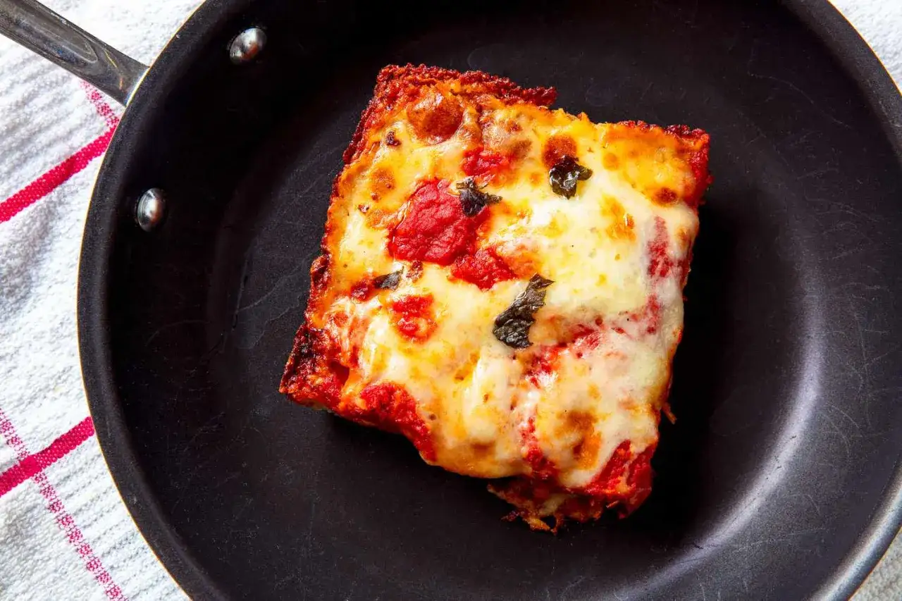 Kawałek pizzy z ciągnącym serem i sosem pomidorowym w czarnej patelni. Idealny spos&oacute;b, jak odgrzać pizzę na patelni, by była chrupiąca.