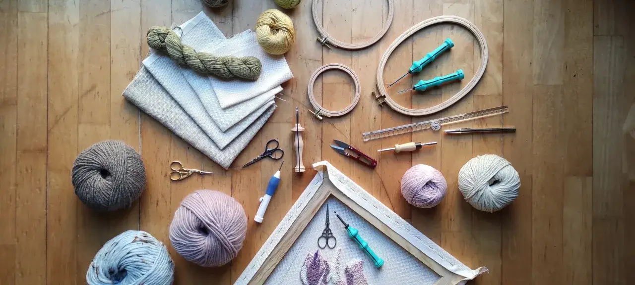 Herramientas para bordar con punz&oacute;n: lanas de colores, telas, bastidores, tijeras y agujas.