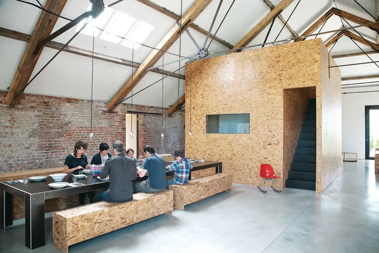 Familie am Esstisch in einem Loft mit rustikalen Ziegelw&auml;nden und einem modernen Innenausbau aus OSB-Platten, die W&auml;rme und Textur verleihen.