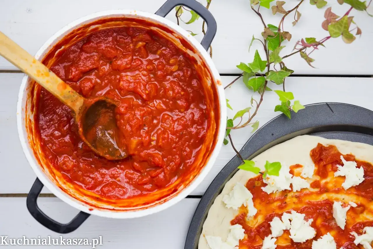 Gęsty, aromatyczny sos do pizzy w garnku, obok surowe ciasto z mozzarellą.