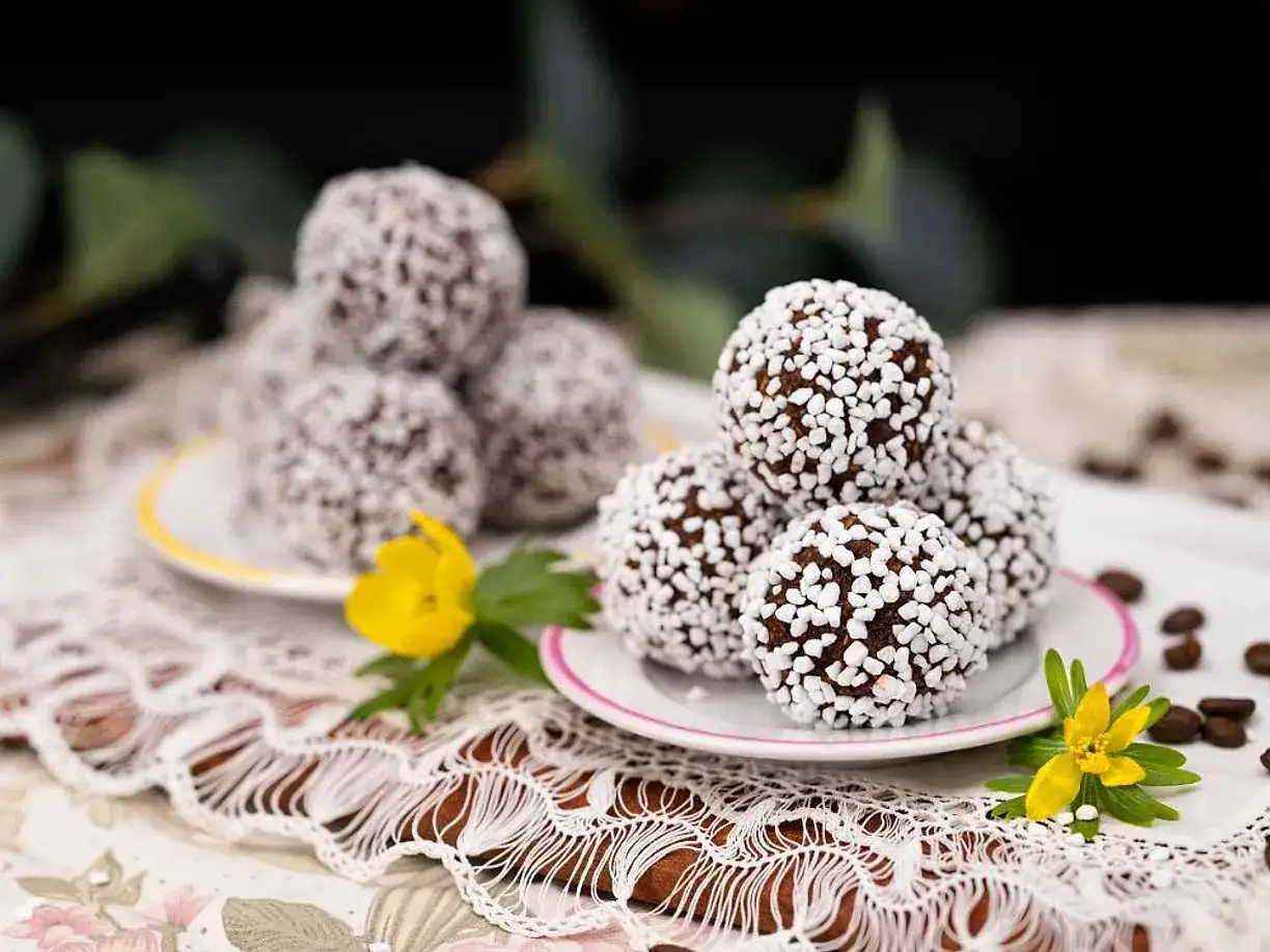 Chokladbollar recept: Mumsiga chokladbollar rullade i p&auml;rlsocker, serverade p&aring; en duk med blommor och kaffeb&ouml;nor.