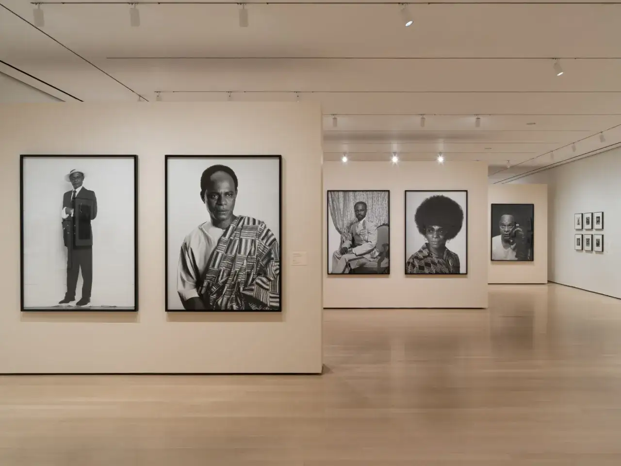 Portraits of famous artists today, including a man in a suit and hat, and another in traditional African attire, displayed in a modern art gallery.