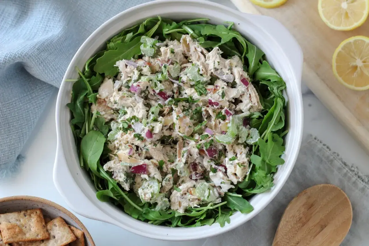 En skål med kyckling sallad, full av selleri, rödlök och örter, serverad på en bädd av ruccola. Perfekt för en lätt lunch.