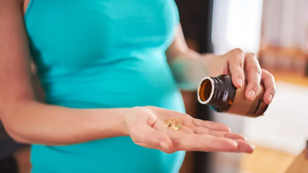 Kobieta w ciąży bierze kapsułki z suplementem. Dba o prawidłowy rozwój dziecka, pamiętając o omega 3 w ciąży.