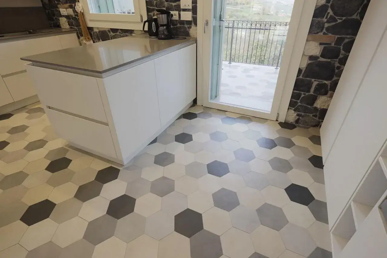 Posa pavimenti esagonali in diverse tonalità di grigio e beige, che creano un motivo geometrico moderno in una cucina luminosa.
