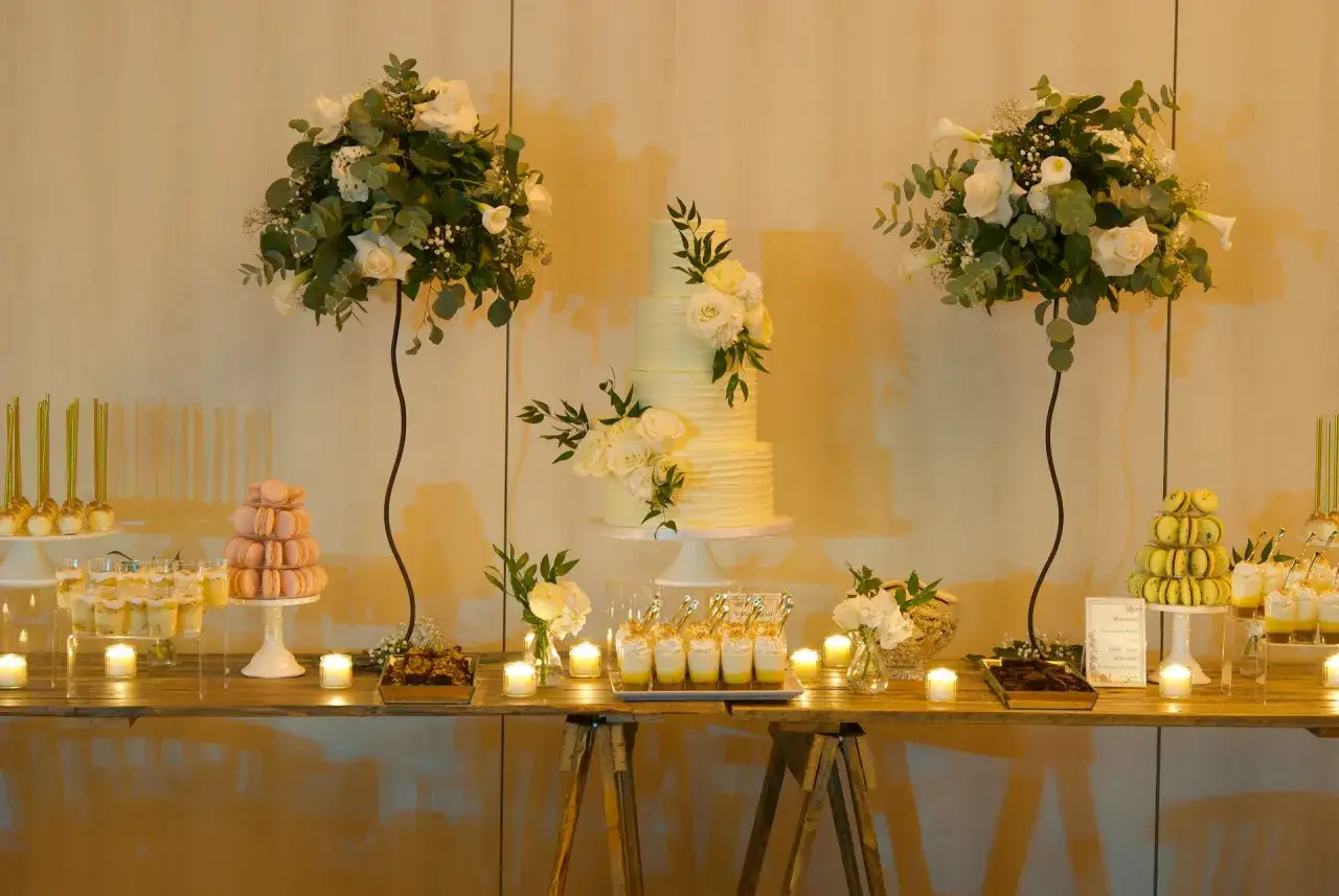 Elegante candy bar boda con pastel de varios pisos, macarons, postres en vasos y arreglos florales blancos.