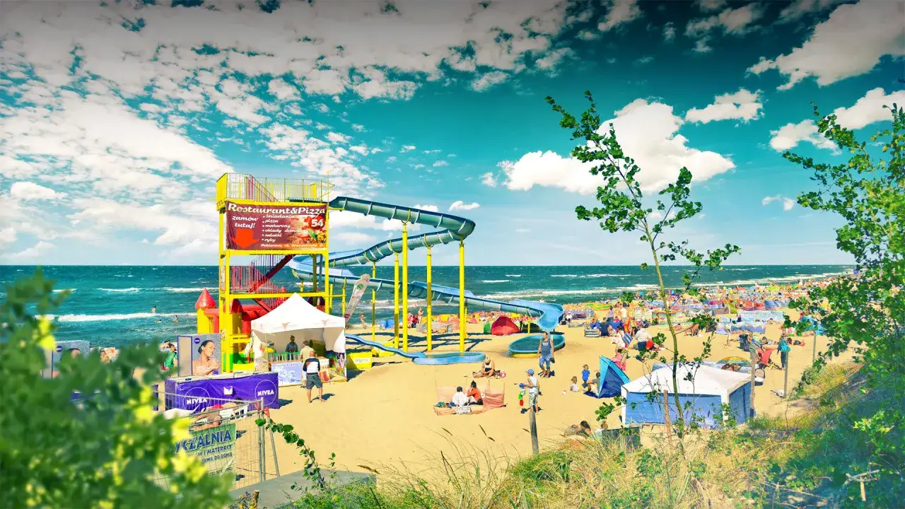 Słoneczny dzień w Pobierowo holiday resort. Dzieci zjeżdżają ze zjeżdżalni wodnych na piaszczystej plaży, a dorośli odpoczywają pod parasolami.