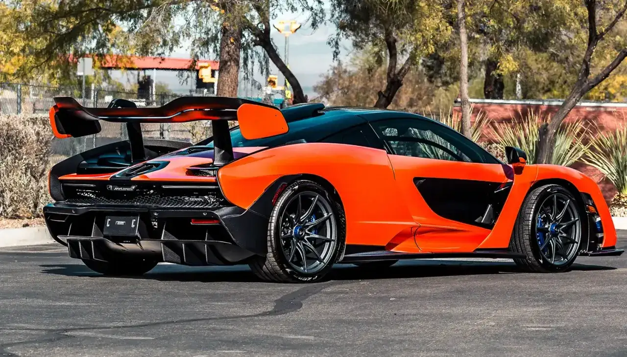 Pomarańczowy McLaren Senna z czarnym dachem i ogromnym skrzydłem, gotowy do wyścigu.