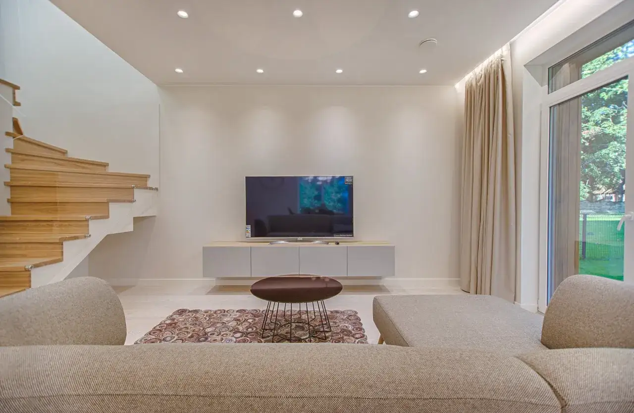 Salon moderne avec escalier en bois, canap&eacute;, t&eacute;l&eacute;vision et un &eacute;l&eacute;gant **plafond tendu** illumin&eacute; par des spots discrets.