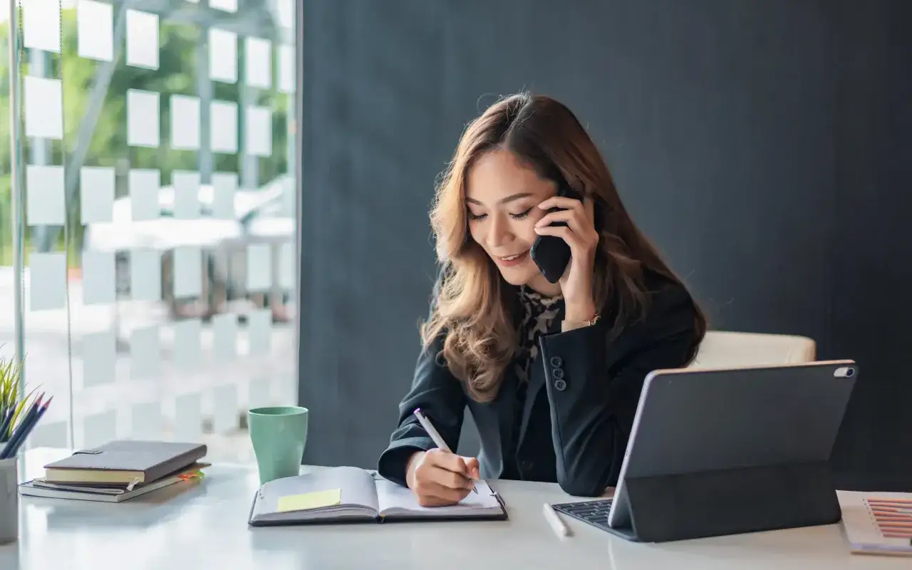 Frau im Büro telefoniert und macht Notizen. Es ist Zeit zum Telefonieren, um wichtige Informationen festzuhalten.