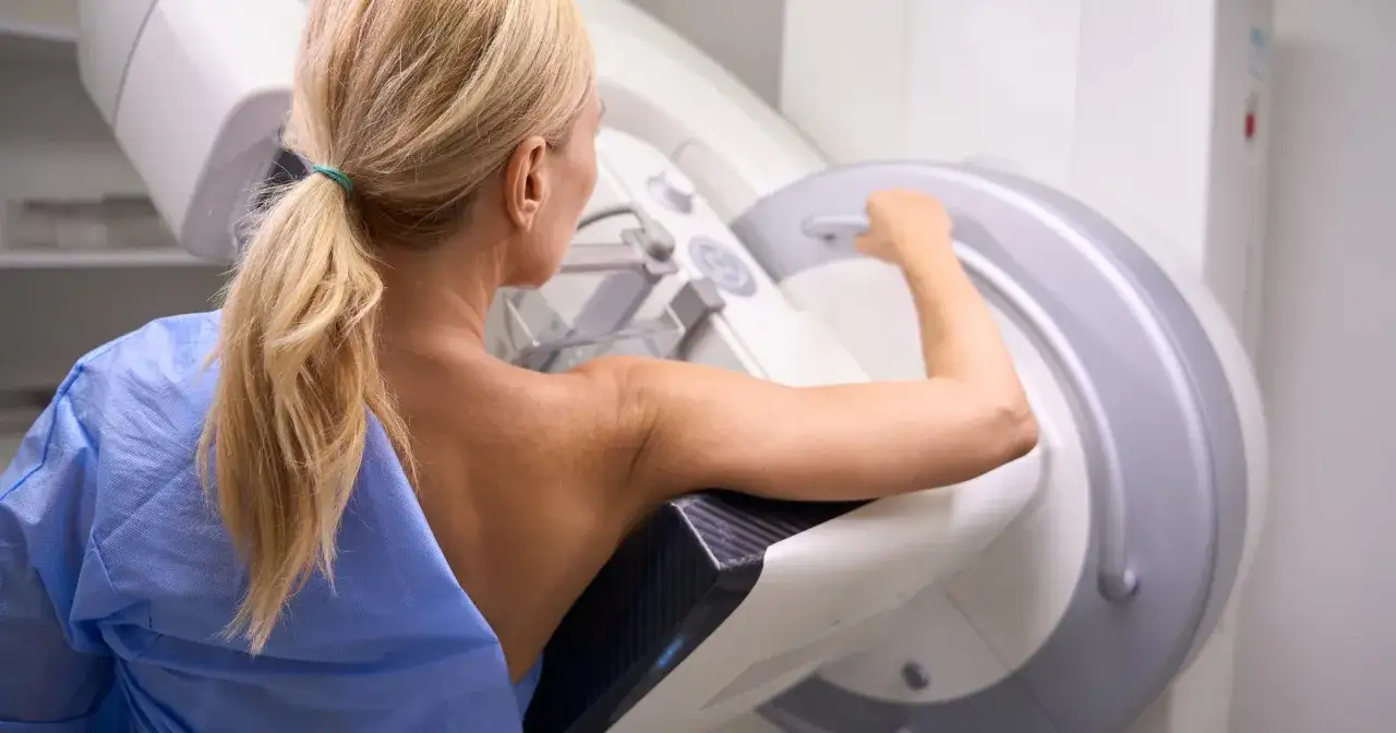 Kobieta w niebieskiej koszuli medycznej poddawana mammografii. Badanie jest rutynowe, ale warto pamiętać o możliwych powikłaniach po mammografii.