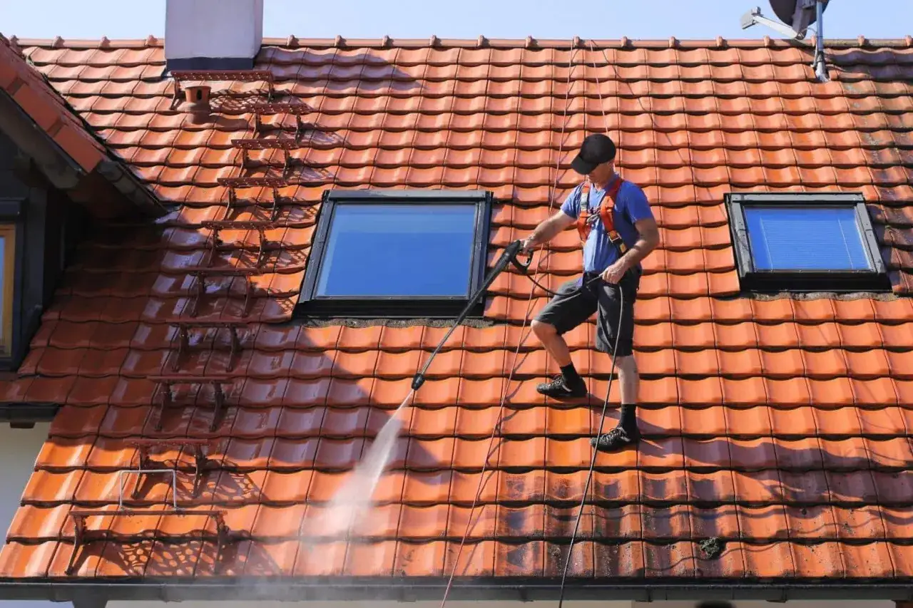 Un couvreur nettoie une toiture en tuiles avec un nettoyeur haute pression. Un bon entretien de toiture assure sa long&eacute;vit&eacute;.