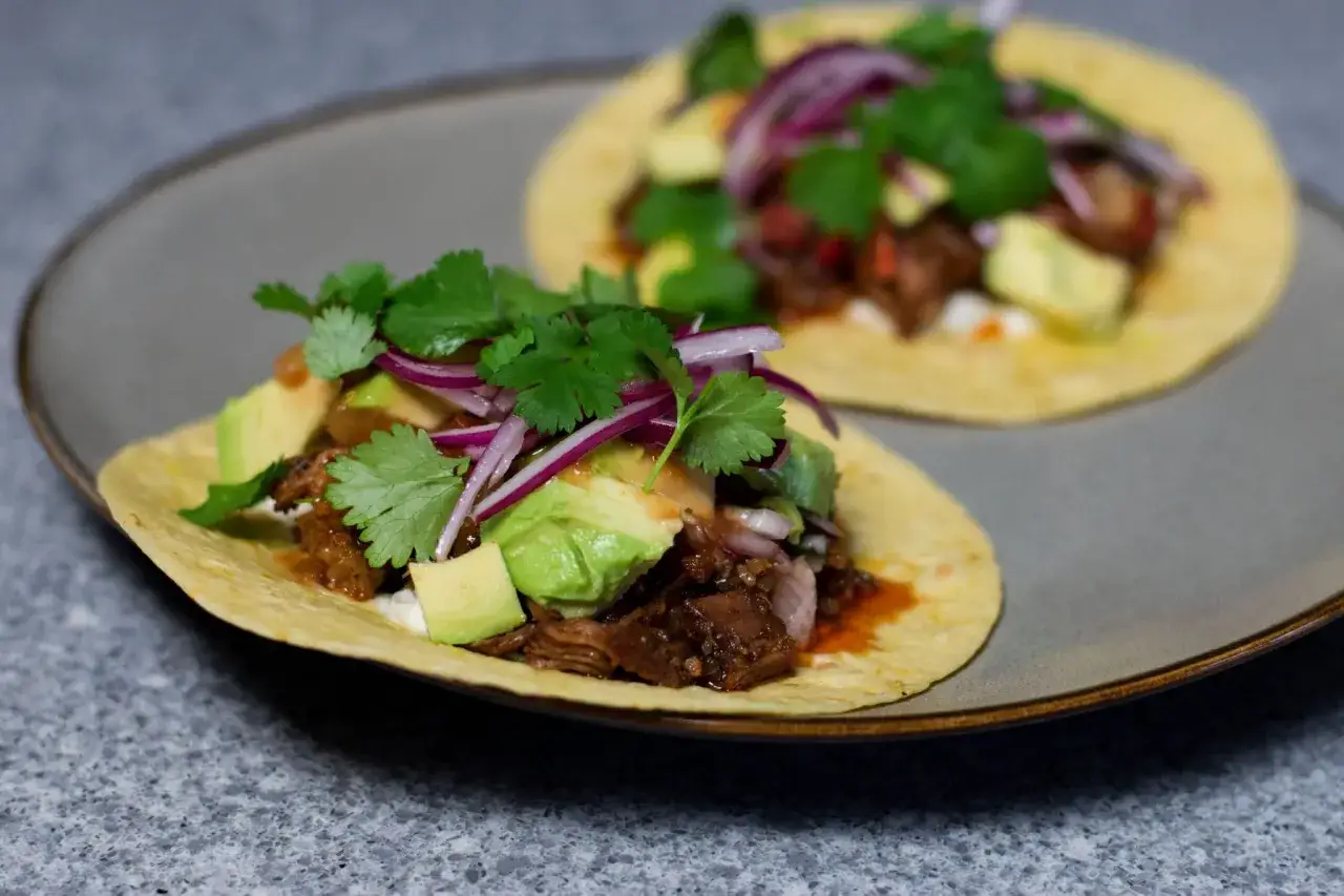 Två läckra carnitas cramby tacos med avokado, rödlök och koriander på en tallrik.