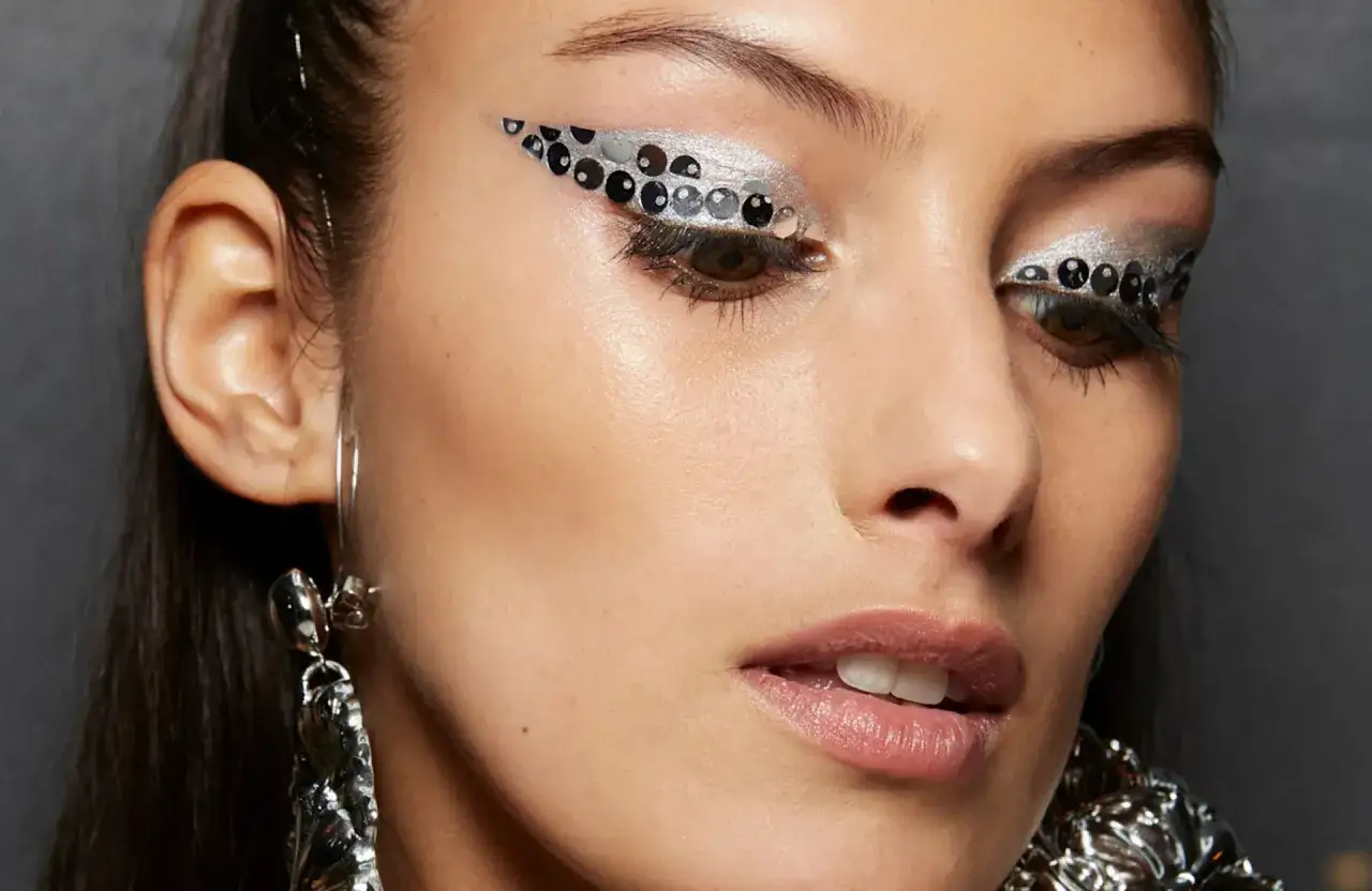 Maquillage yeux Noël facile : un regard scintillant avec des paillettes argentées et des sequins noirs formant un œil de chat audacieux.