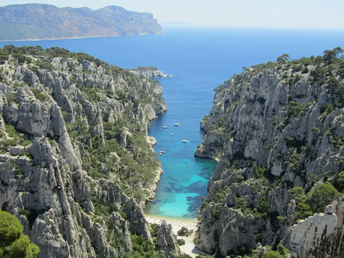 Vue spectaculaire depuis le belvédère d'En Vau, avec ses falaises calcaires plongeant dans une eau turquoise où quelques bateaux naviguent. Une petite plage est visible au fond.