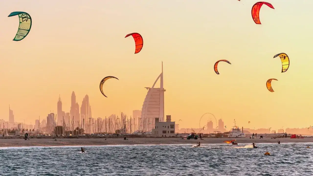 Kolorowe latawce unoszą się nad plażami w Dubaju, gdzie kitesurferzy korzystają z fal przy zachodzącym słońcu.