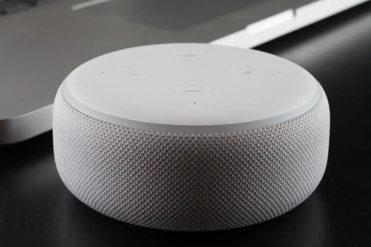 Biały głośnik Echo Dot z włączoną funkcją Alexa język polski, obok laptopa.