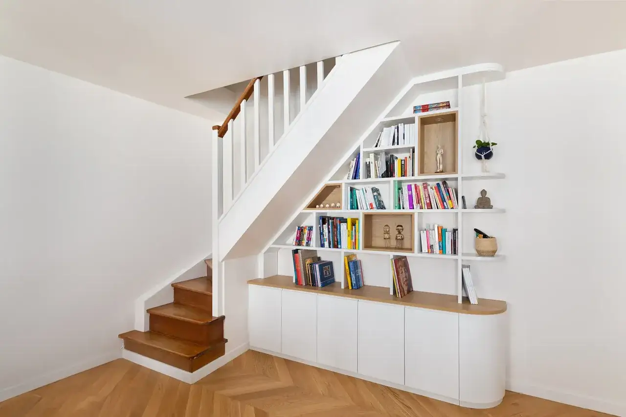 Am&eacute;nagement cage d'escalier avec &eacute;tag&egrave;res murales et rangements bas, optimisant l'espace sous l'escalier.