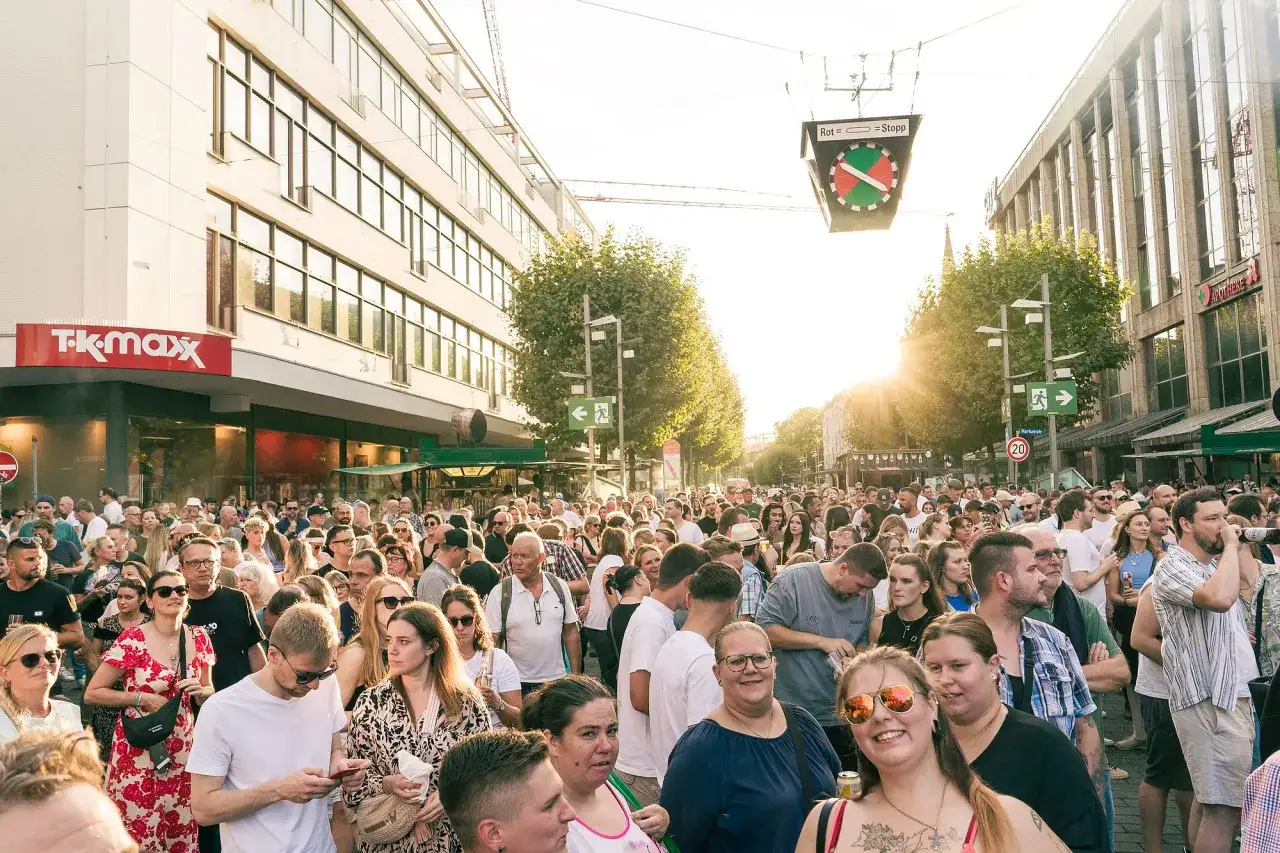 Menschenmenge feiert bei kostenlosen Veranstaltungen in Bochum. Die Sonne scheint, ein Verkehrssignal h&auml;ngt &uuml;ber der Stra&szlig;e.