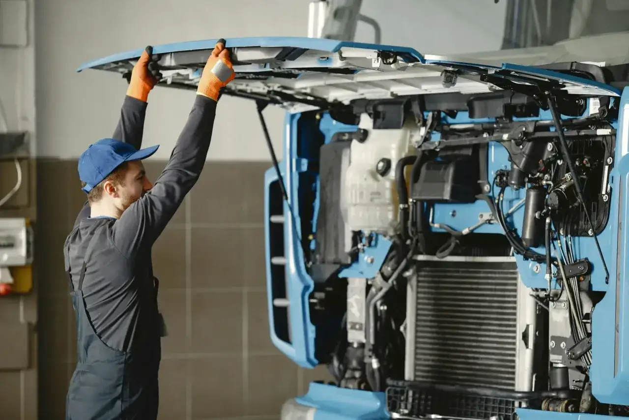 Mechanik w pomarańczowych rękawicach podnosi maskę ciężarówki, by sprawdzić, czy nie ma stukania przy dodawaniu gazu.