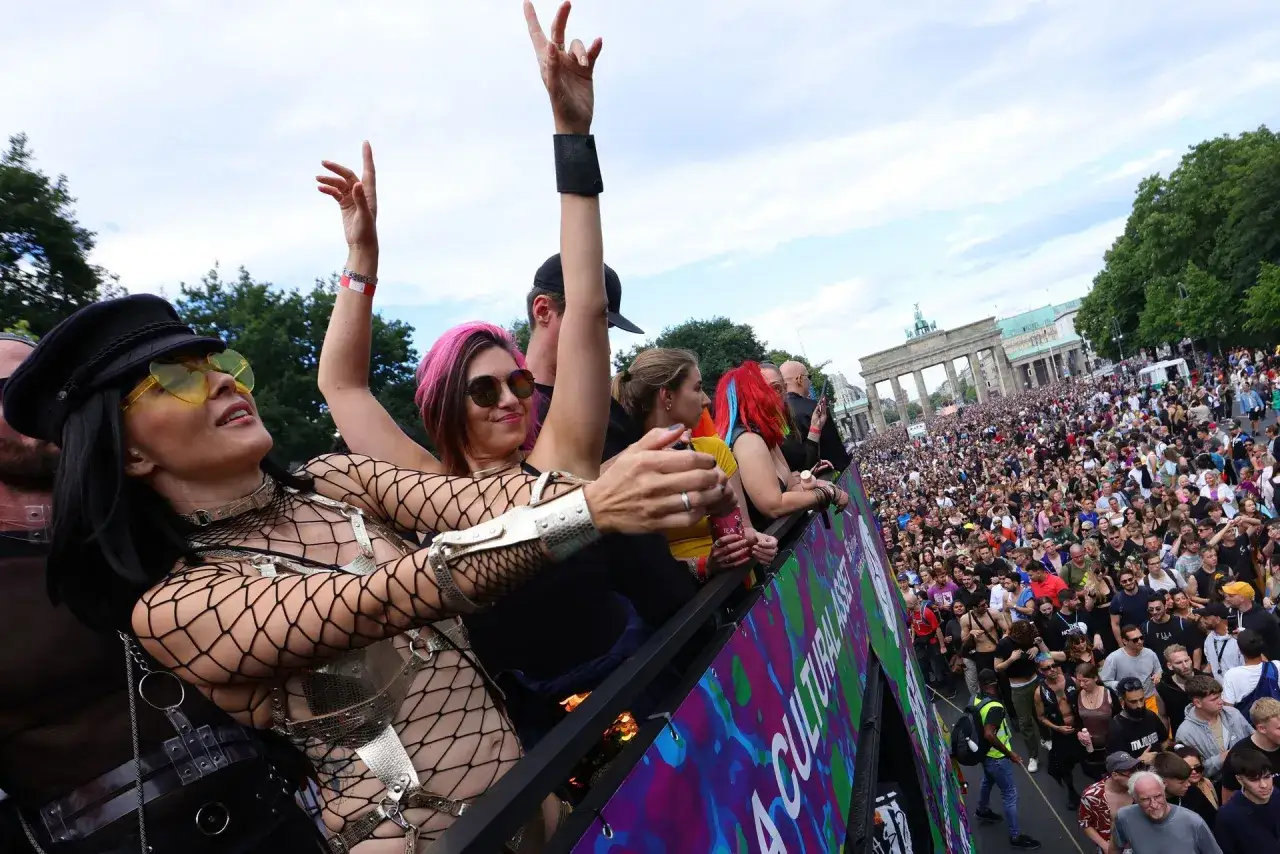Tłum świętuje na Love Parade pod Bramą Brandenburską. Ludzie na platformie w ekstazie, w tle tłumy i zabytkowa budowla.